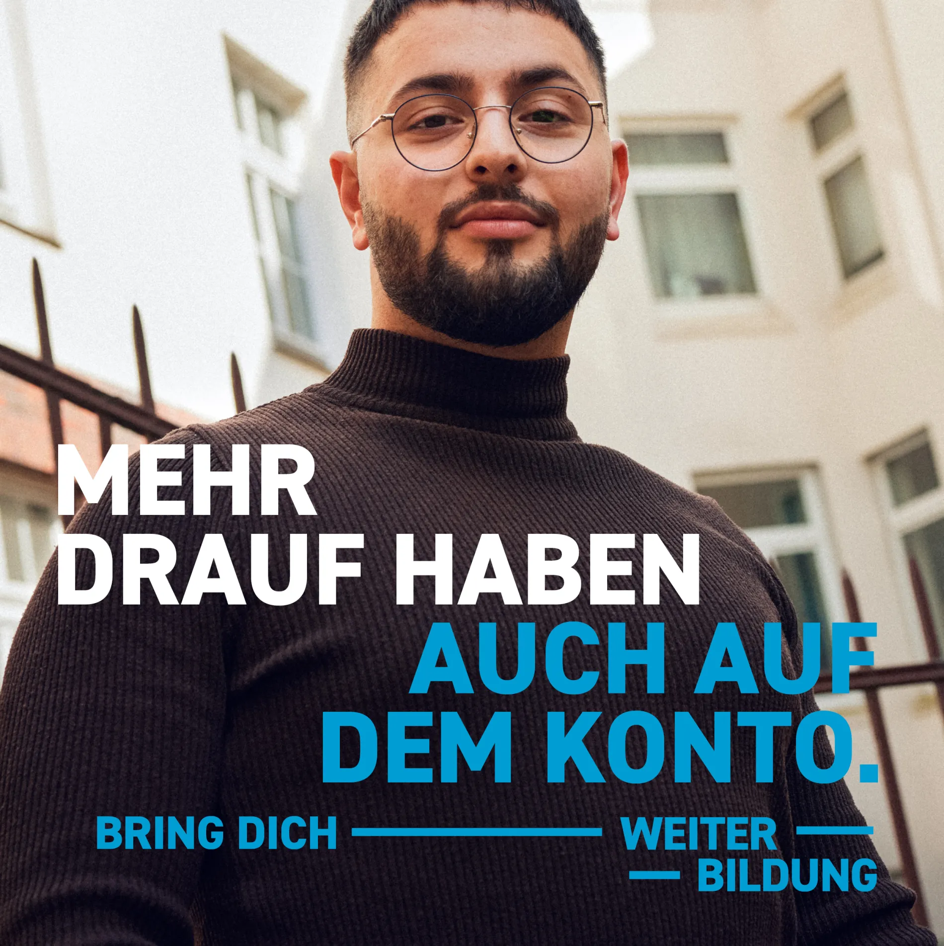 Ein junger Mann mit kurzen schwarzen Haaren, schwarzem Bart und Brille lächelt freundlich. Er trägt einen braunen Rollkragenpullover. Text im Bild: „Mehr drauf haben. Auch auf dem Konto. Bring dich weiter. Bildung.“